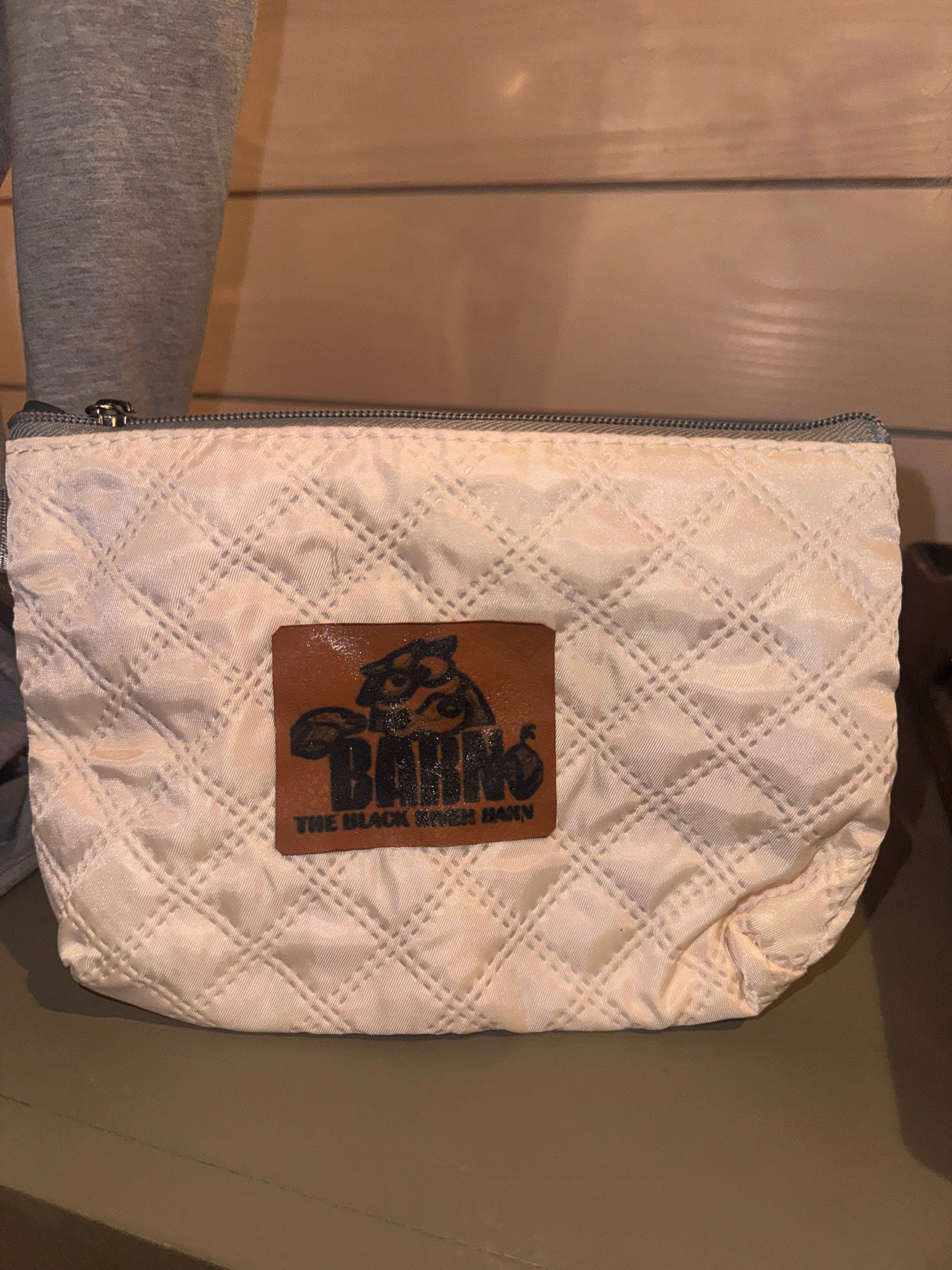 Quilted white Black River Barn makeup bag with logo patch and zipper closure
